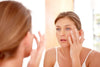 Blue-eyed woman looking in mirror and applying organic skincare